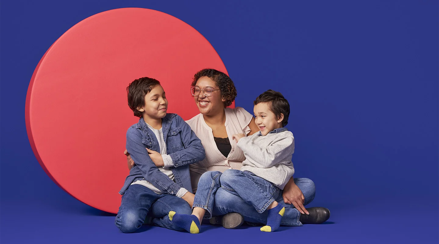 Still of a mother and two children against a pink circle and purple background.