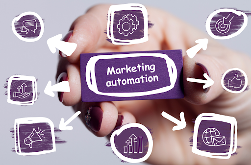 Hand holding a badge that reads "Marketing Automation" with illustrated marketing icons including graphs, gears, bullseyes, envelopes, etc.