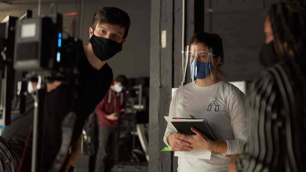 Anne Mulaire_InclusiveSizingBTS Man and woman looking at a camera screen with masks on