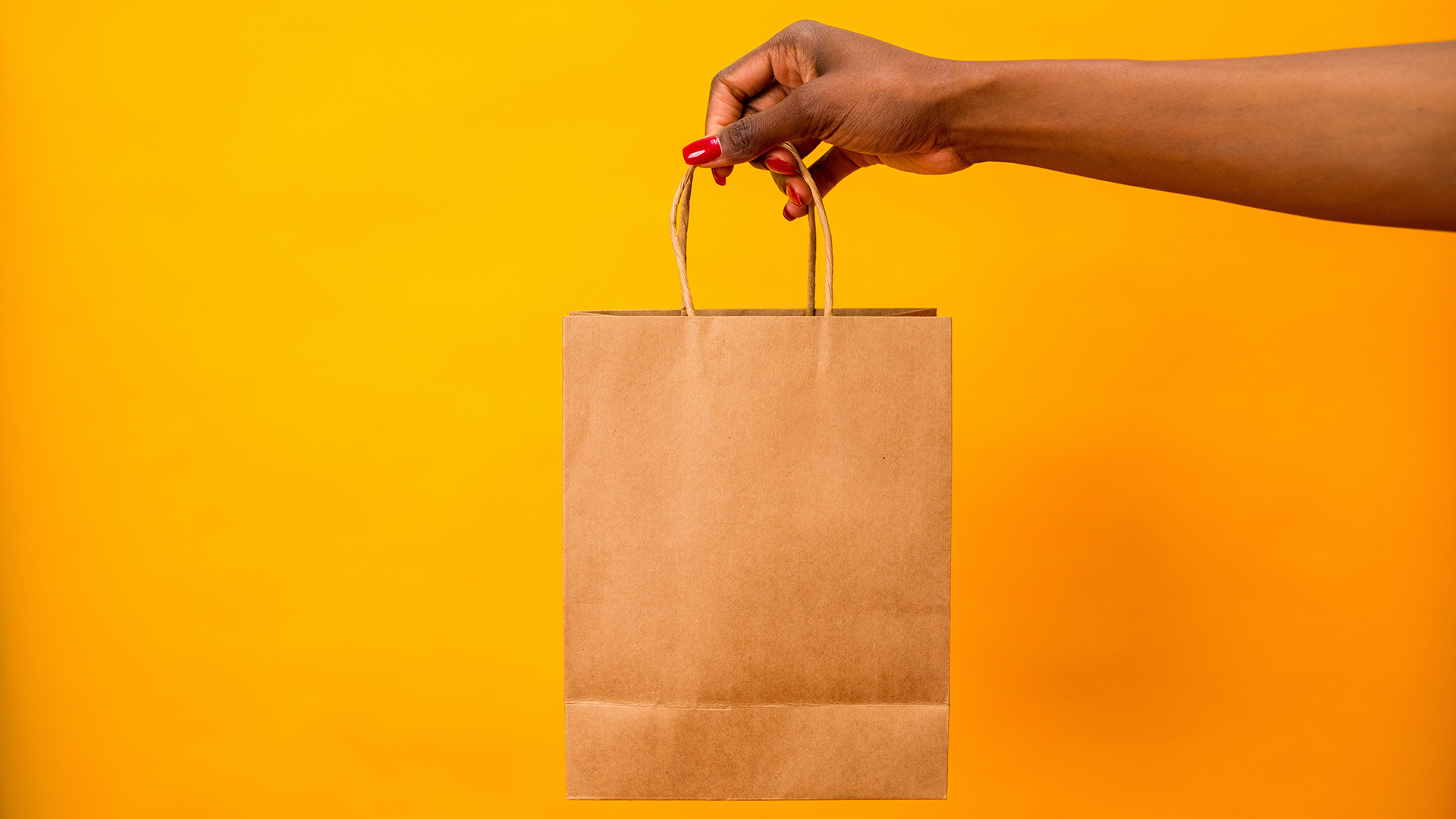 Hand holding a brown paper bag in front of a bright yellow background.