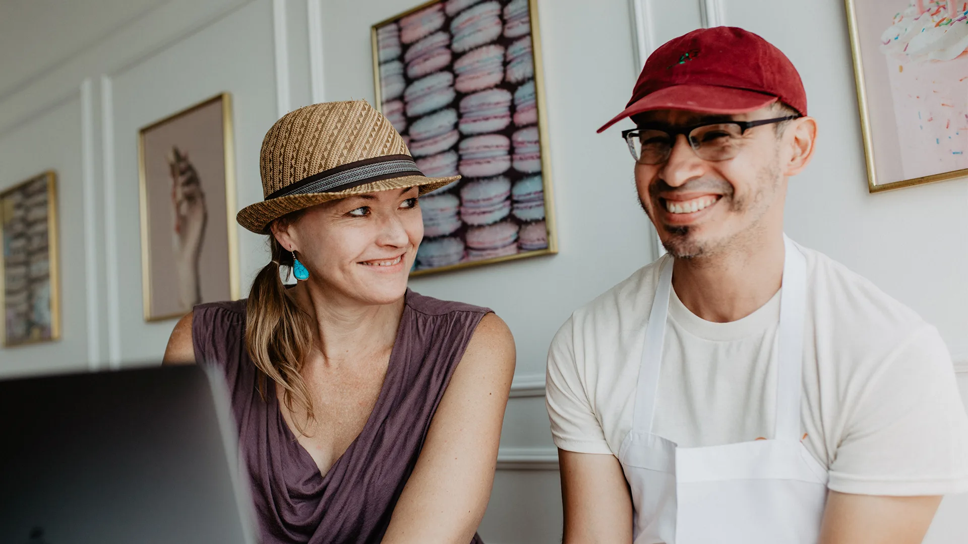 Two people sitting in a cafe in front of a laptop.