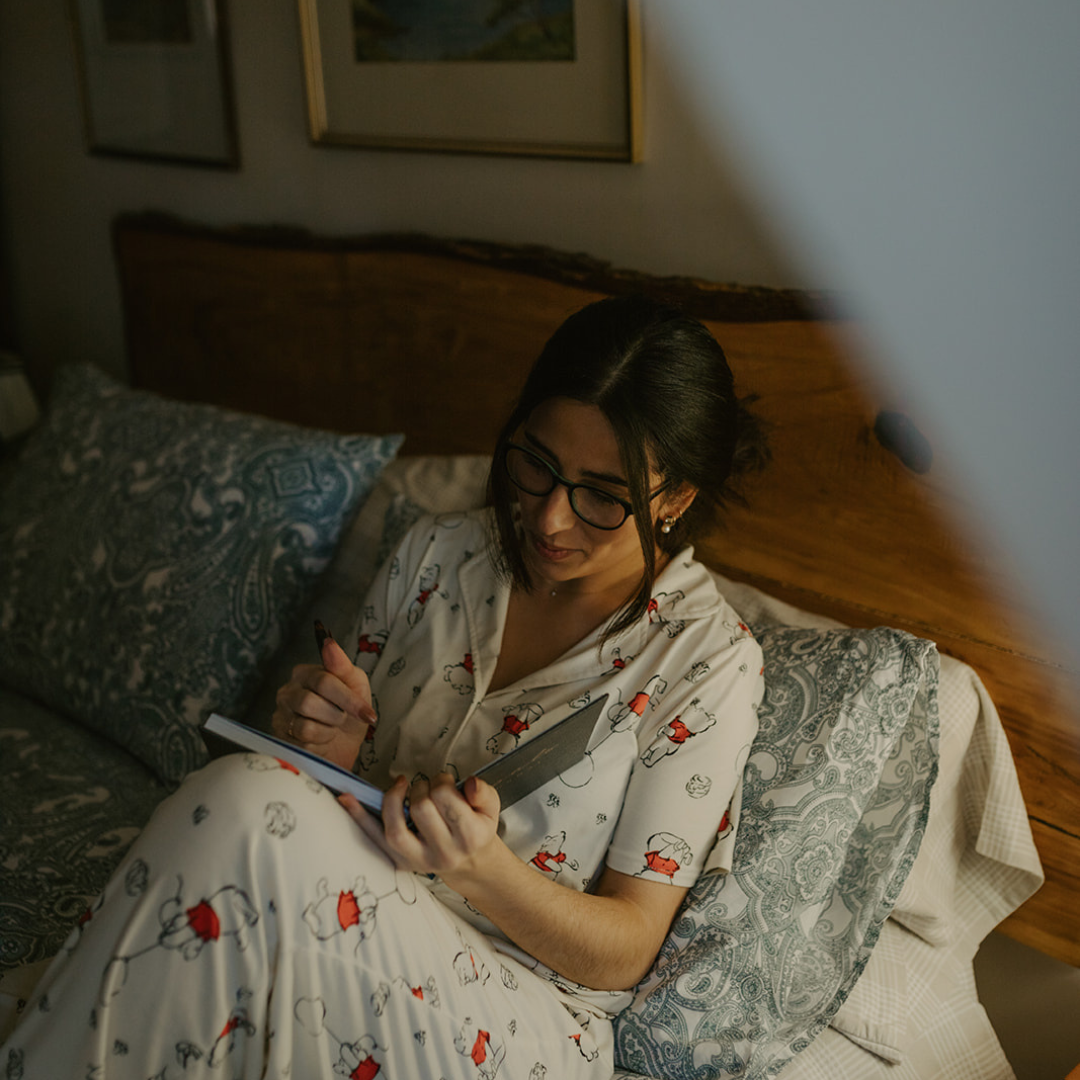 Patricia Gomez in pajamas, laying in bed writing in a journal.