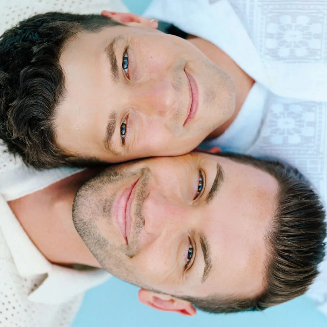 Matthew and Micheal laying in opposite directions with cheeks touching as they smile into the camera.