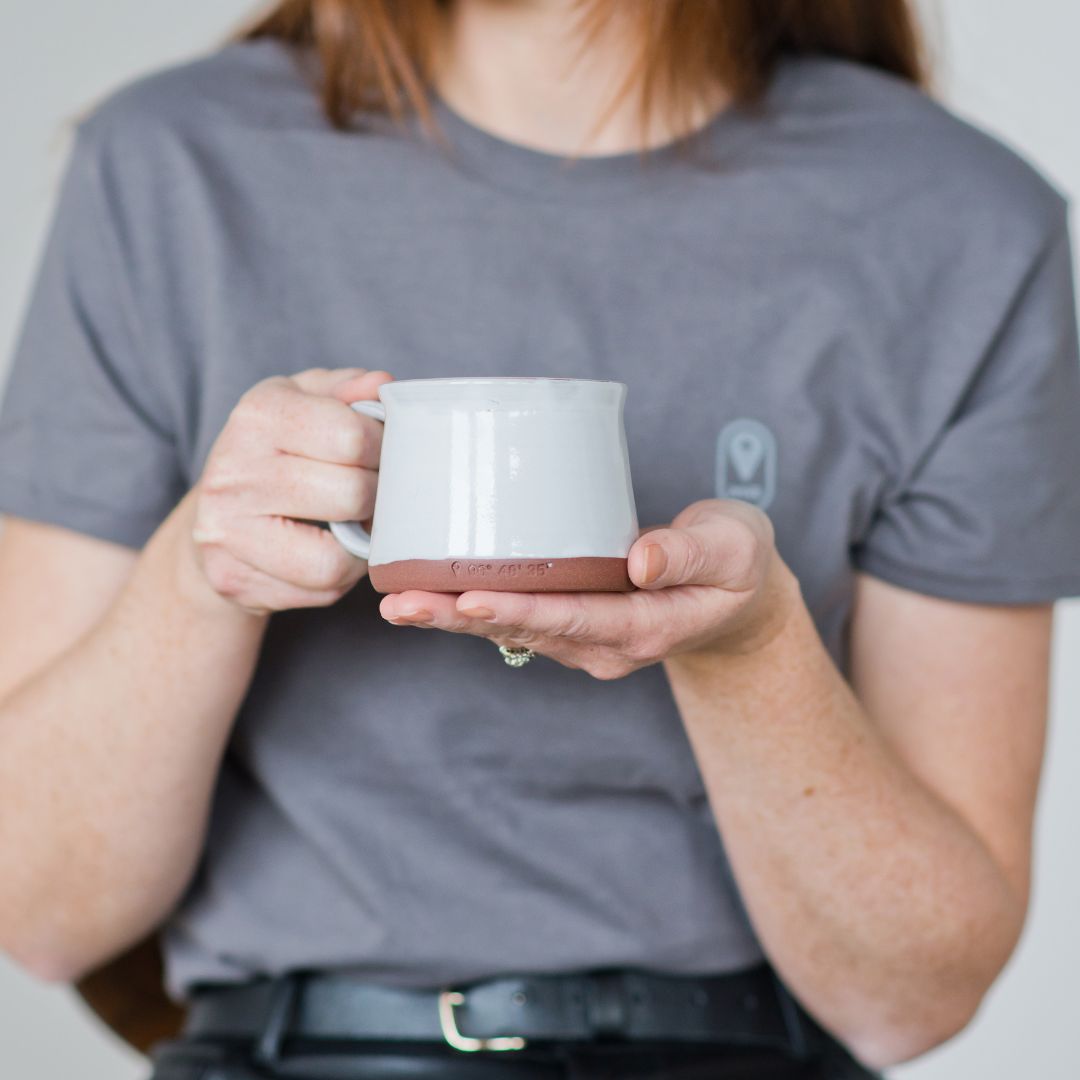 A person in a Travel Manitoba shirt holding a limited edition Manitoba ceramic mug.
