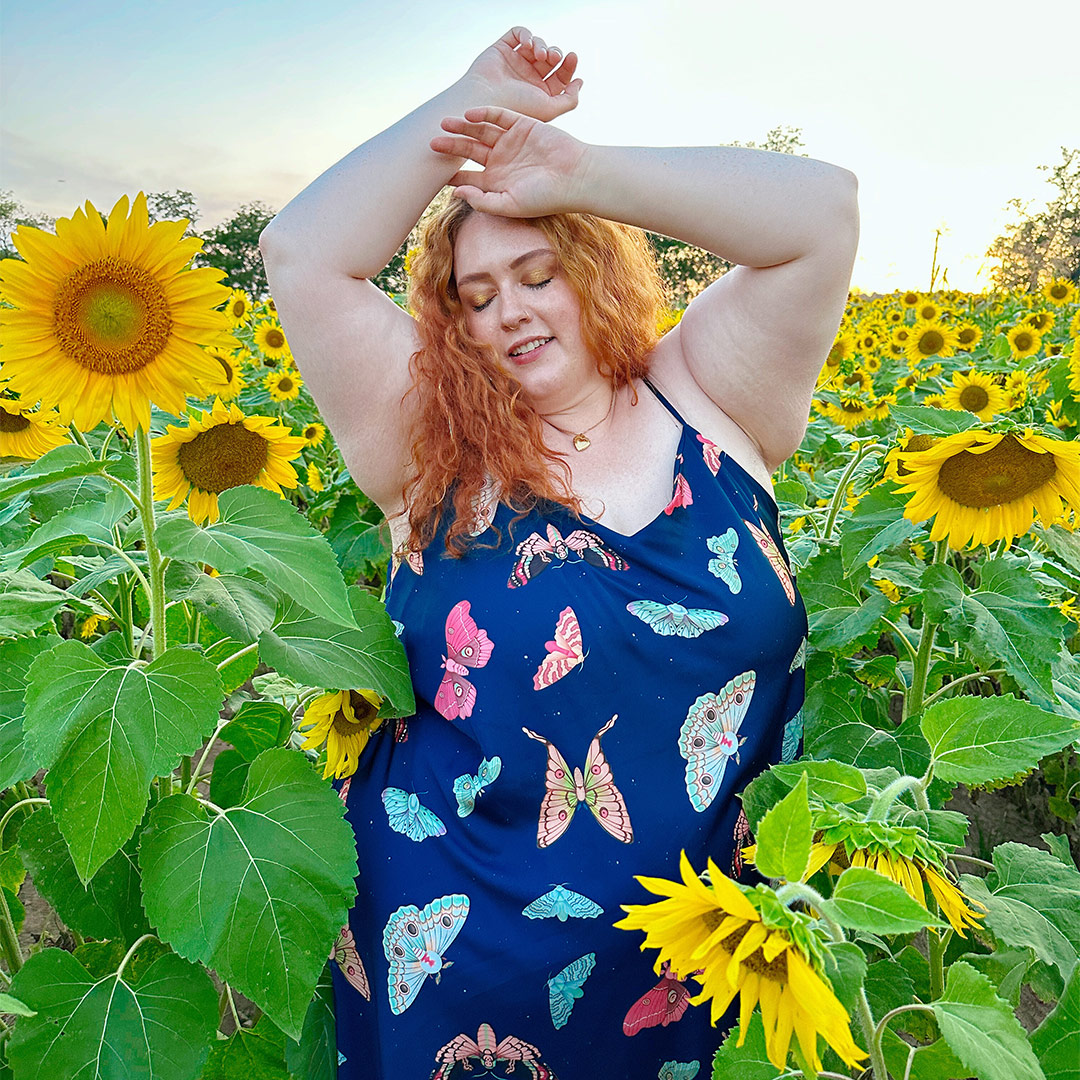 Kimmy Garris posing in a sundress amongst a field of sunflowers.