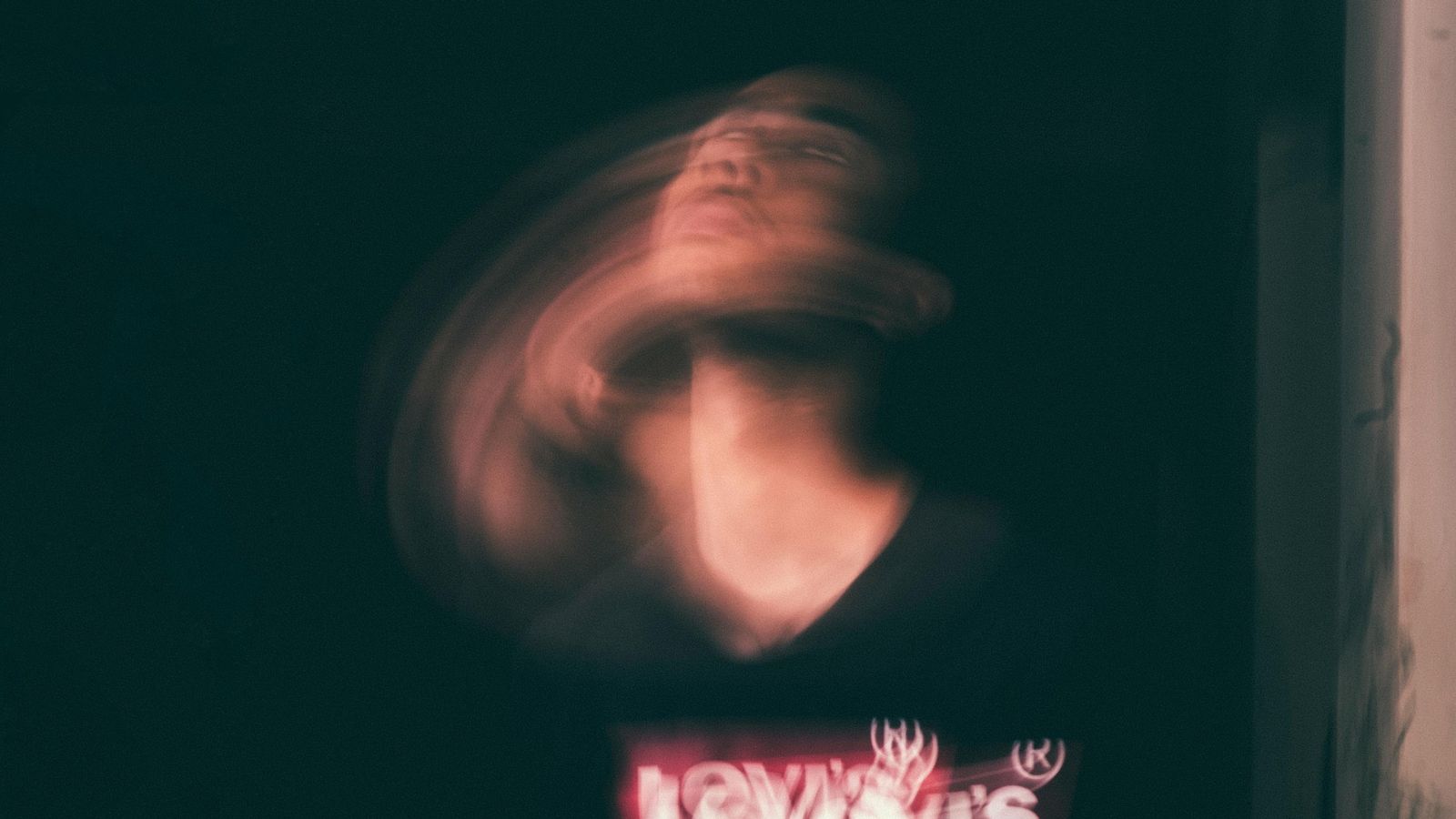 A photograph taken with a long exposure to capture a blurred image of a person's head shaking violently.