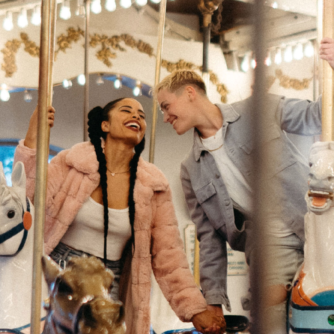 Ruby and Katrina laughing with each other while riding a merry-go-round.