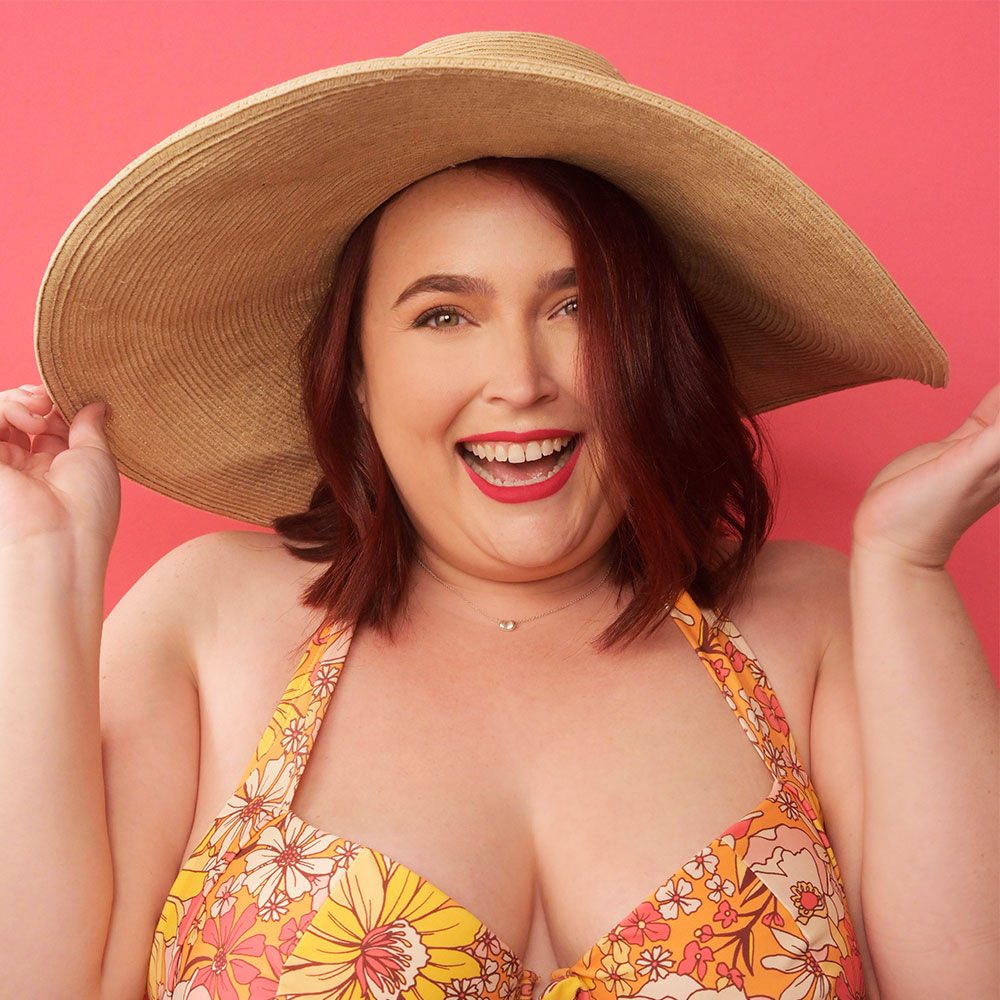 Lauren wearing a wide-brim straw hat and a colorful floral bikini top, set against a vibrant pink background.