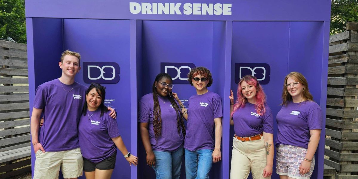 Scott and other brand ambassadors wearing DrinkSense shirts and standing in front of an outdoor DrinkSense booth.