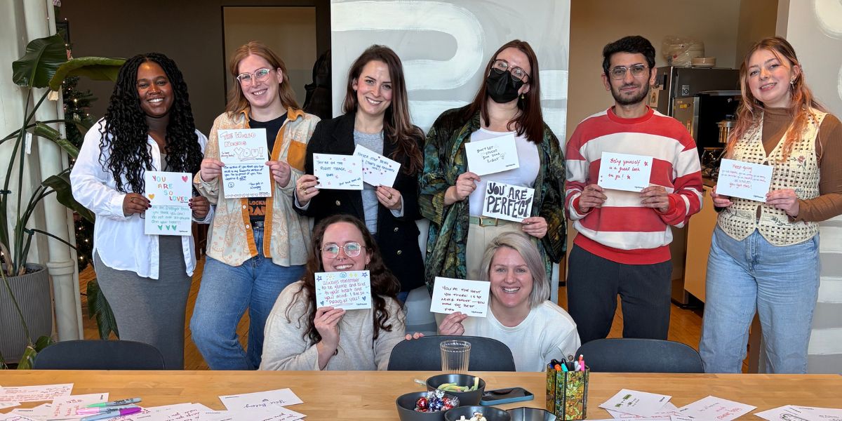 UpHouse staff standing at the kitchen table showing off the cards they wrote for the Point of Pride card signing project, supporting trans youth.