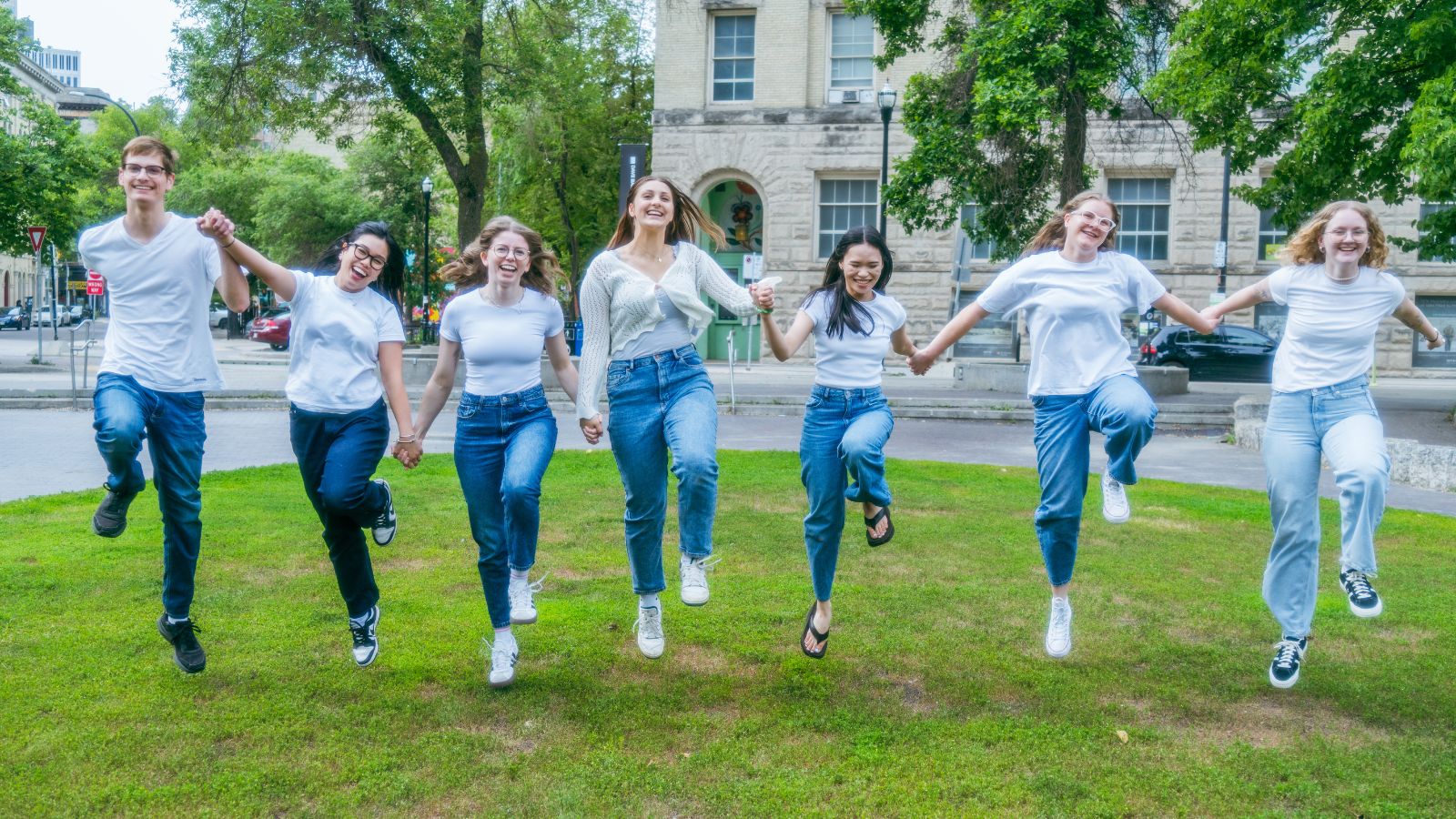 1 Seven people skipping through grass while holding hands and smiling.