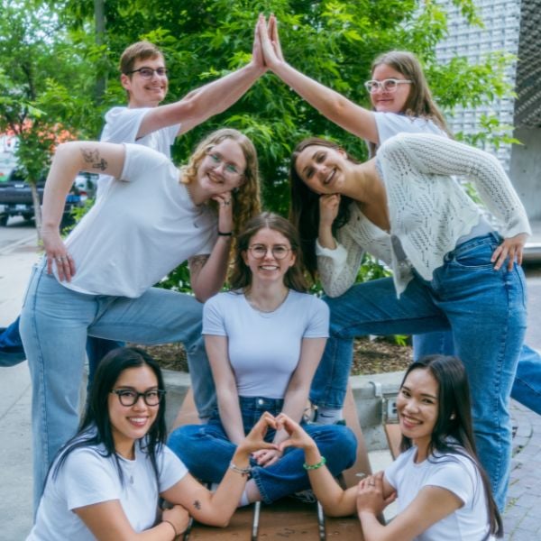 Seven people wearing white tops and jeans posing on a picnic table.