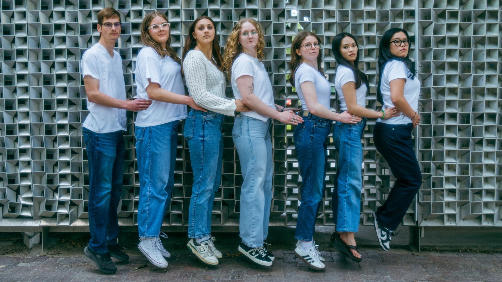 3 Seven people wearing white tops and jeans jumping with serious faces.